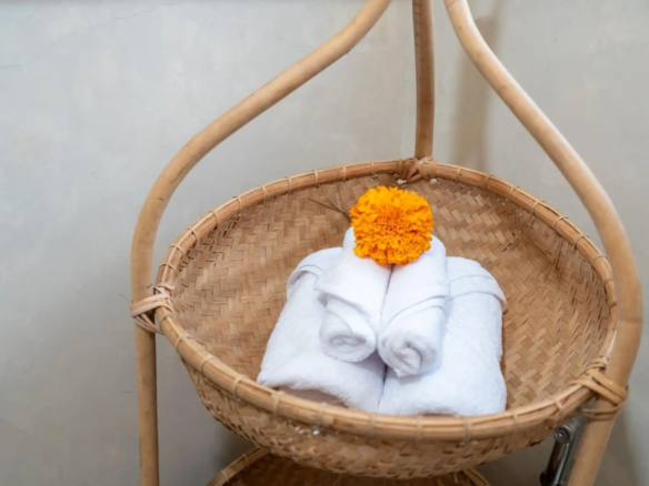 Wicker chair with a white towel folded into a flower shape and an orange marigold on top for a spa look.