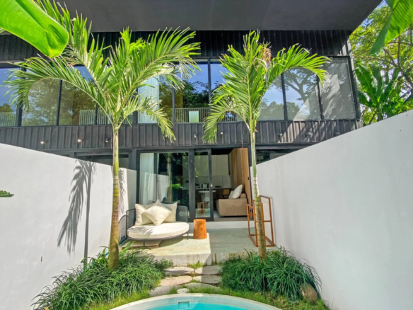 Modern outdoor courtyard with tall palm trees, glass doors, and a round cushioned seating area by a small pool.