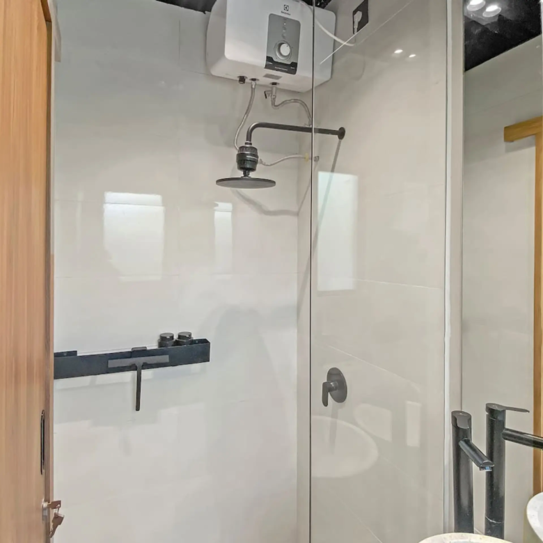 Bathroom interior featuring a glass shower enclosure, rainfall shower head, and wall-mounted water heater; wooden doors and grey tiled walls.