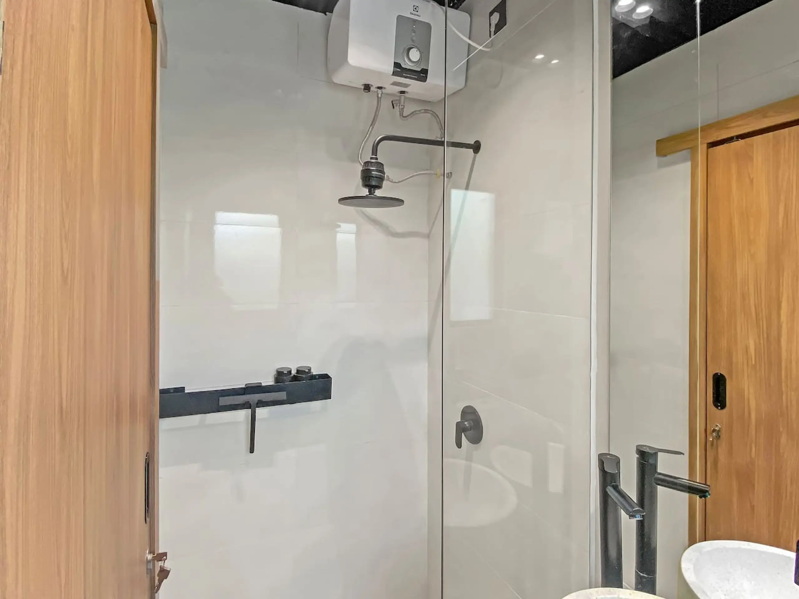 Bathroom interior featuring a glass shower enclosure, rainfall shower head, and wall-mounted water heater; wooden doors and grey tiled walls.
