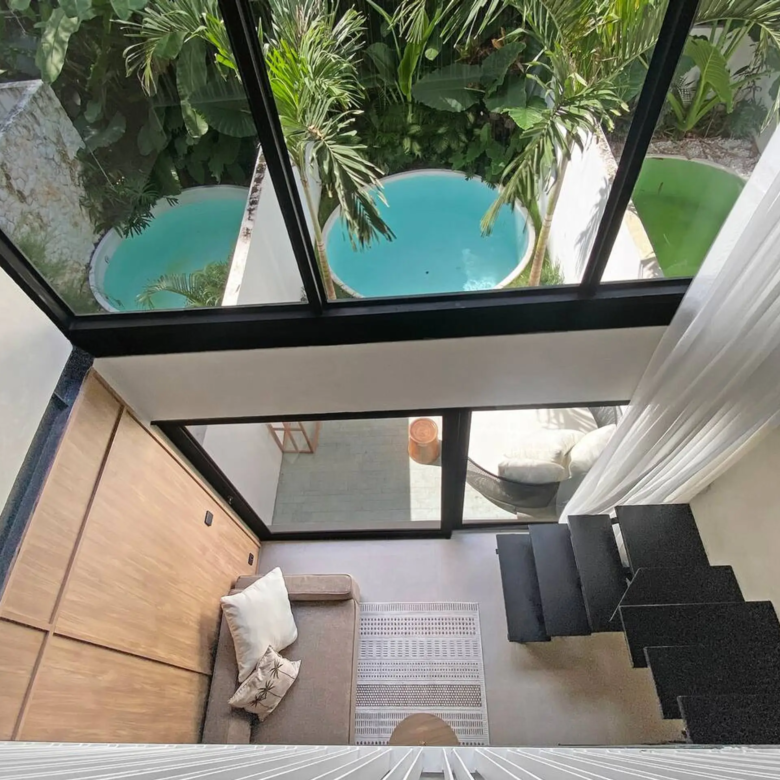 Modern stairwell and seating area seen through large glass walls with tropical plants outside.