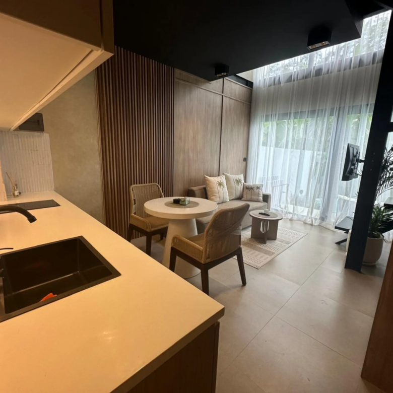 Contemporary open-plan kitchen and living area with an island, sink, and pillowed seating by large windows with sheer curtains.