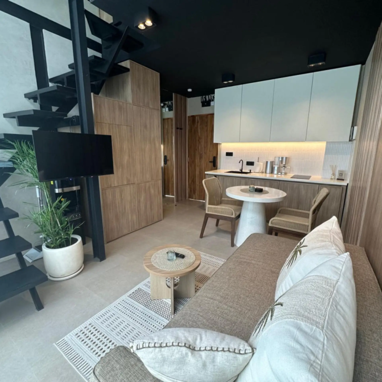 Modern living area with a black metal staircase, wood cabinets, white countertops, and a beige sofa with throws; green plant in a white pot nearby.
