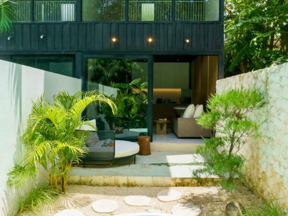 Modern black house with large glass walls and tropical plants, viewed from a circular turquoise pool in the foreground.