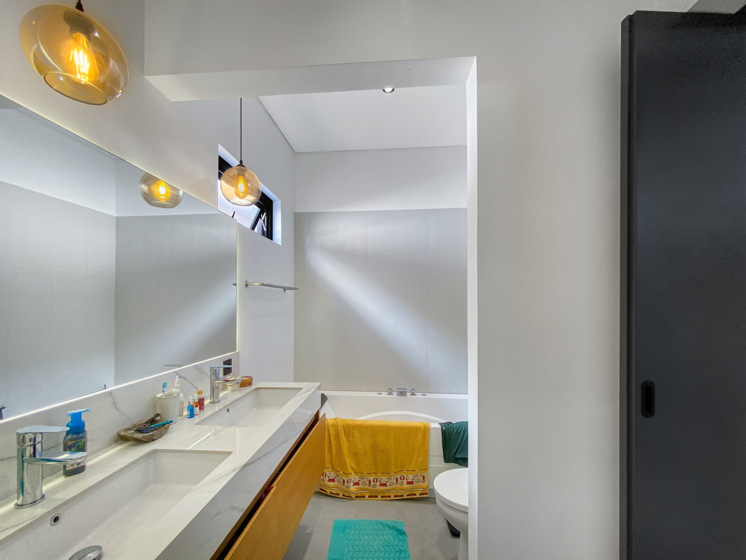 Modern bathroom with double white sink, marble countertop, and amber glass pendant lights.