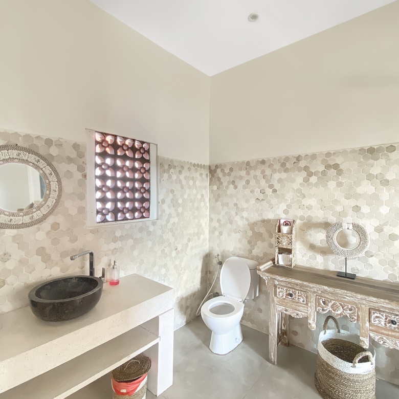 Bathroom with beige hex tile walls, round wicker-framed mirror, open vanity counter, and white toilet.