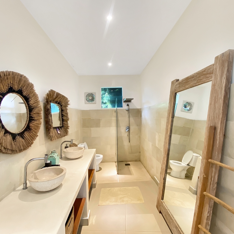 Bathroom with two stone sinks on a long counter, woven circular mirrors, and a wooden ladder mirror setup.