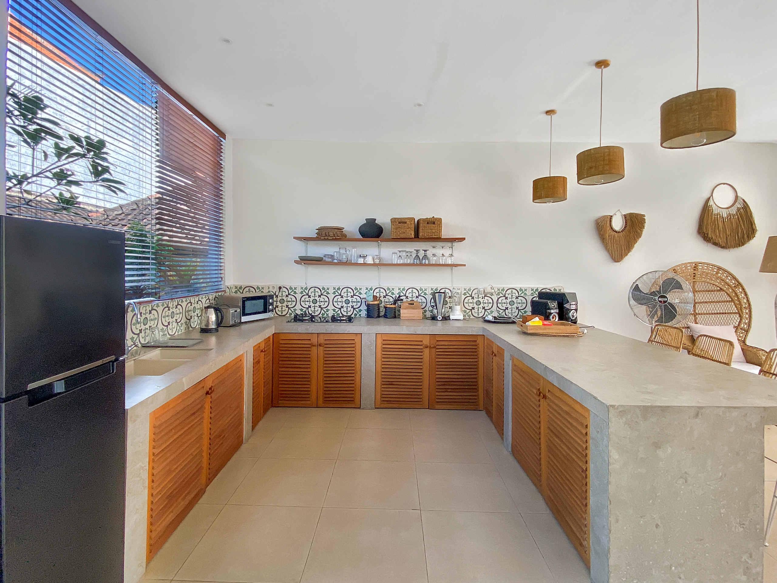 Bright kitchen with wooden cabinets, patterned tile backsplash, open shelves, and warm pendant lights.