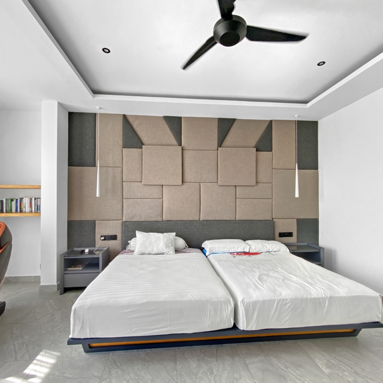Modern hotel bedroom with padded beige/gray headboard wall, two single beds, and a ceiling fan overhead.