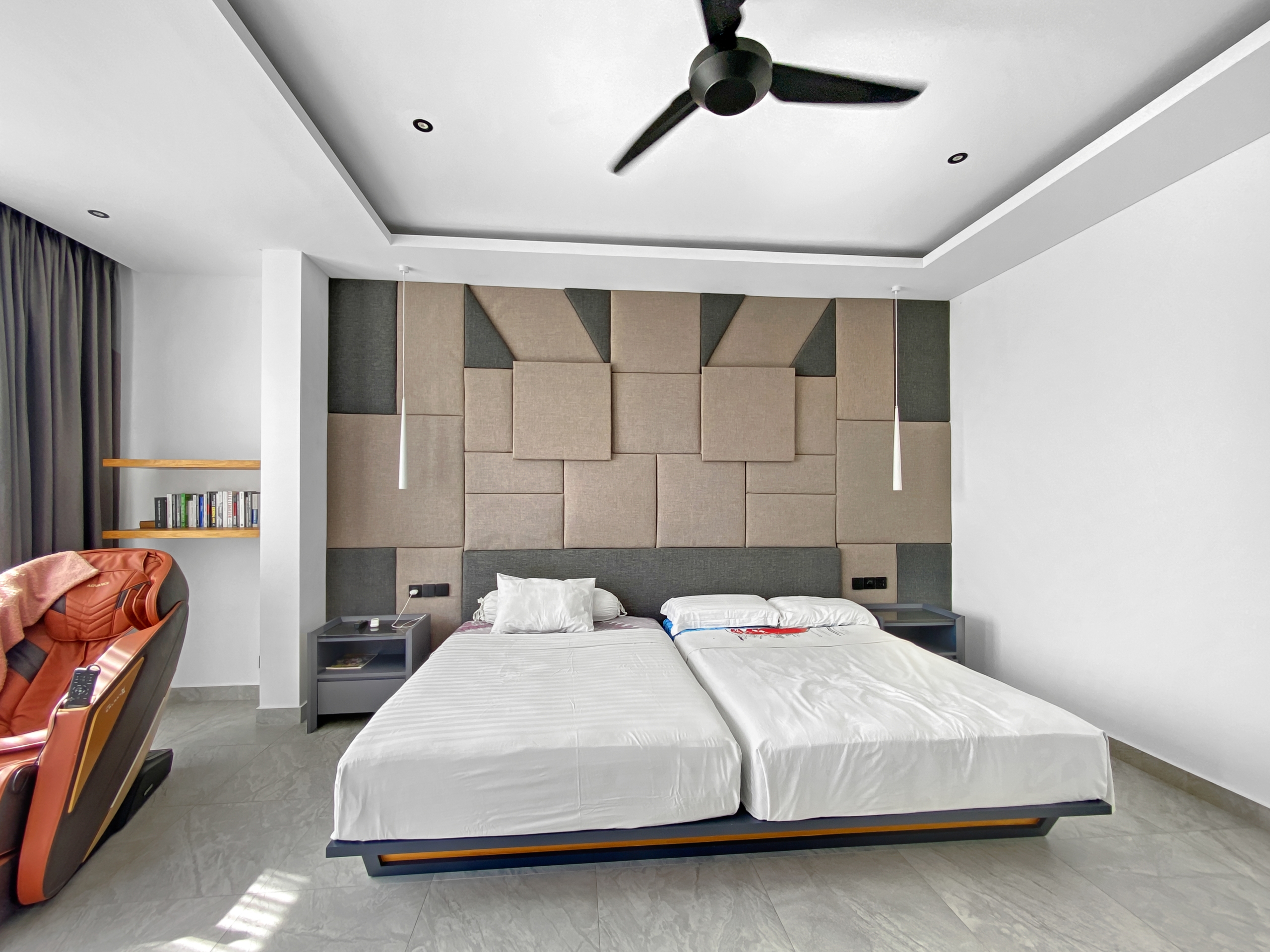 Modern hotel bedroom with padded beige/gray headboard wall, two single beds, and a ceiling fan overhead.