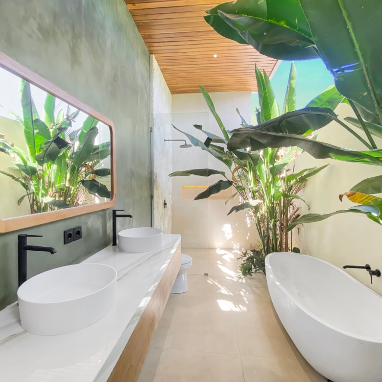Modern bathroom with white freestanding tub, double vessel sinks, black fixtures, and large tropical plants near a green wall.