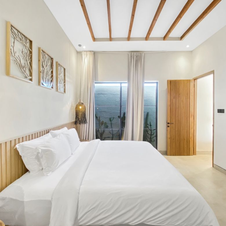Bright hotel bedroom with white bedding, wooden slatted headboard, and exposed ceiling beams