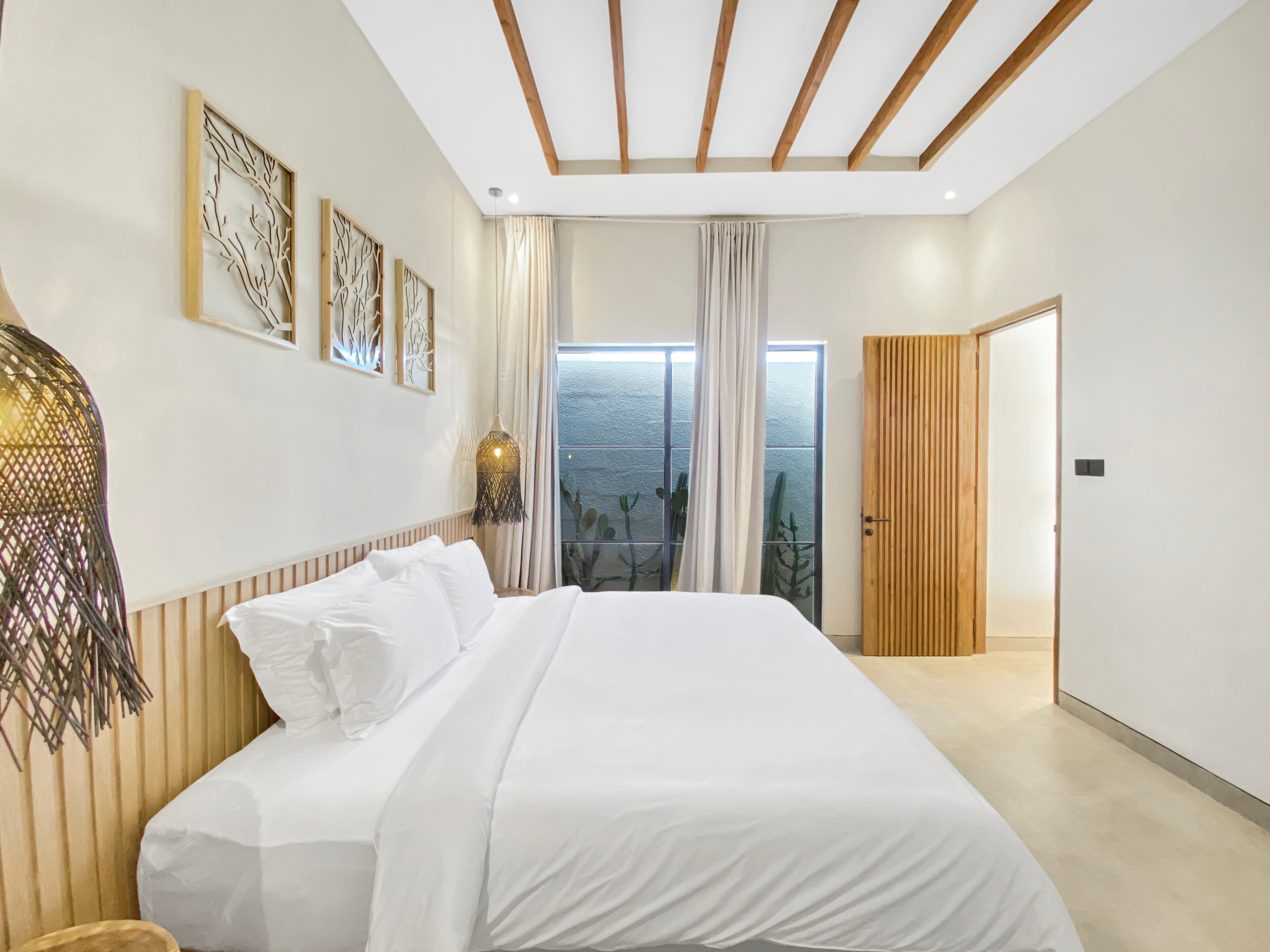 Bright hotel bedroom with white bedding, wooden slatted headboard, and exposed ceiling beams