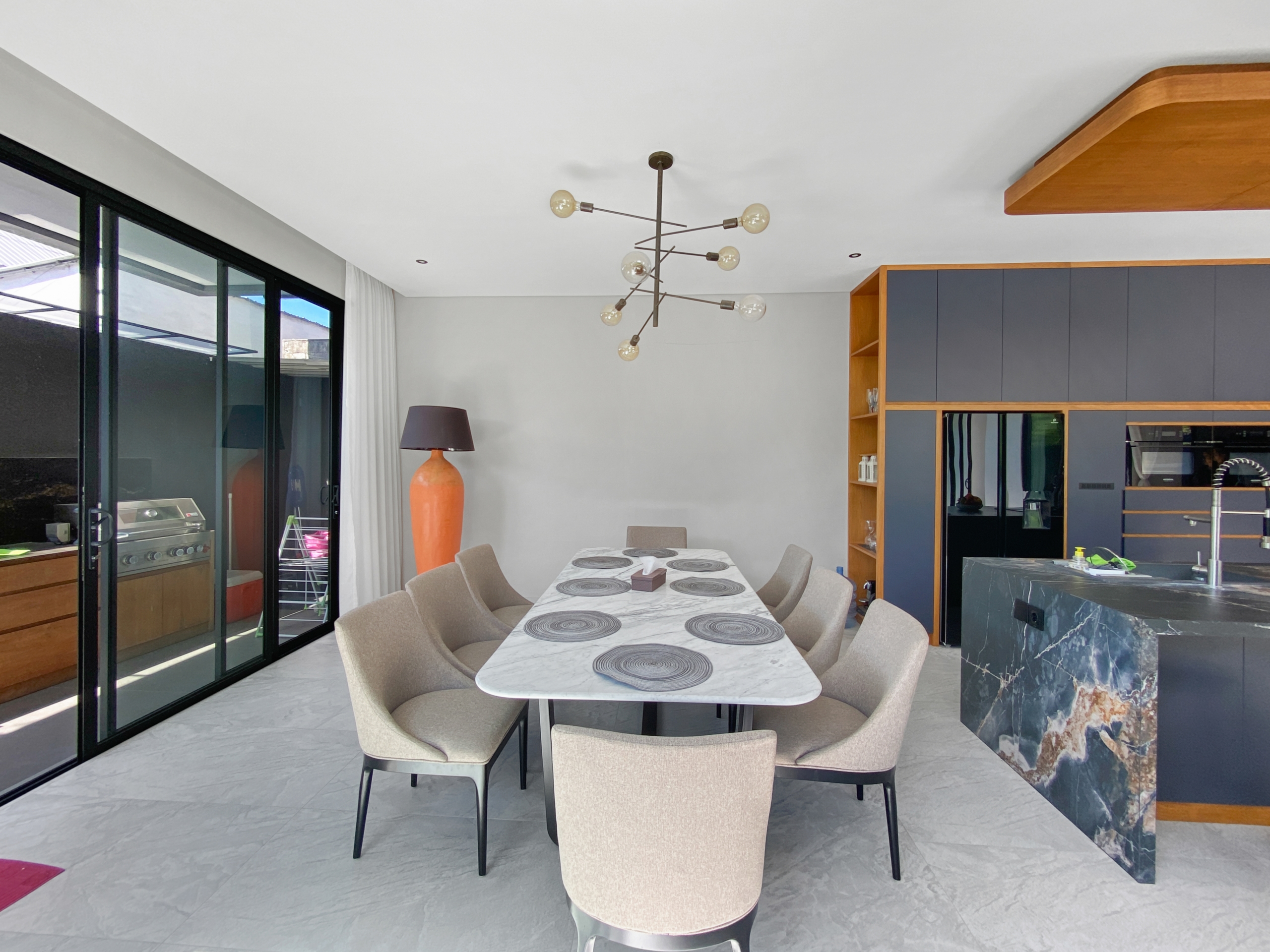 Modern kitchen-dining area with a marble table set for six, beige upholstered chairs, and a starburst chandelier overhead.