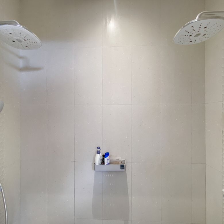 Shower enclosure with two large round ceiling rain showerheads and a handheld wand on the left wall.