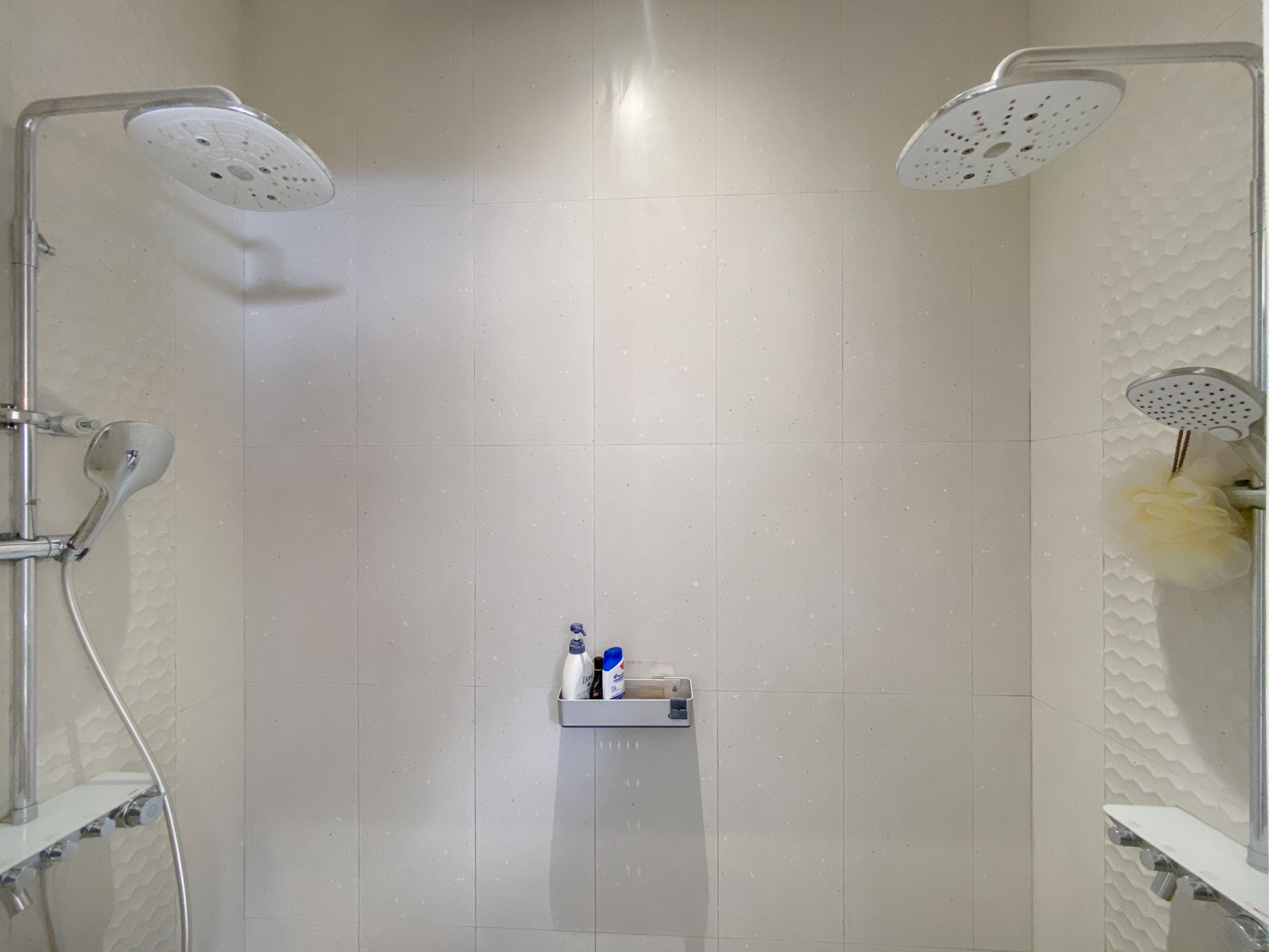 Shower enclosure with two large round ceiling rain showerheads and a handheld wand on the left wall.