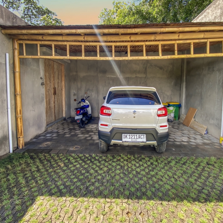 White SUV parked inside a bamboo-framed carport against gray walls.