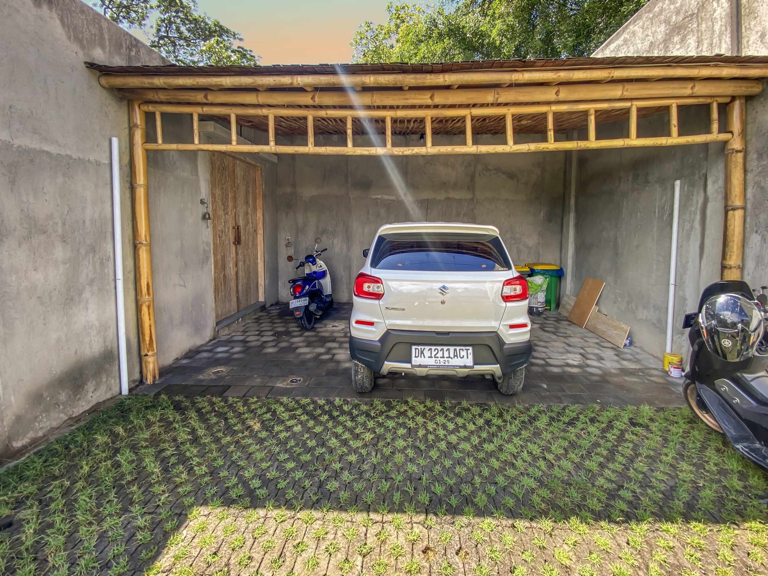 5fecdcb645aad274de4a9f49eba34d2aa054a2a7 White SUV parked inside a bamboo-framed carport against gray walls.