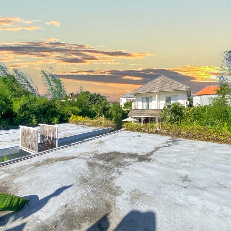 Rooftop terrace with white railings and lush greenery, overlooking suburban houses at sunset." (concise)