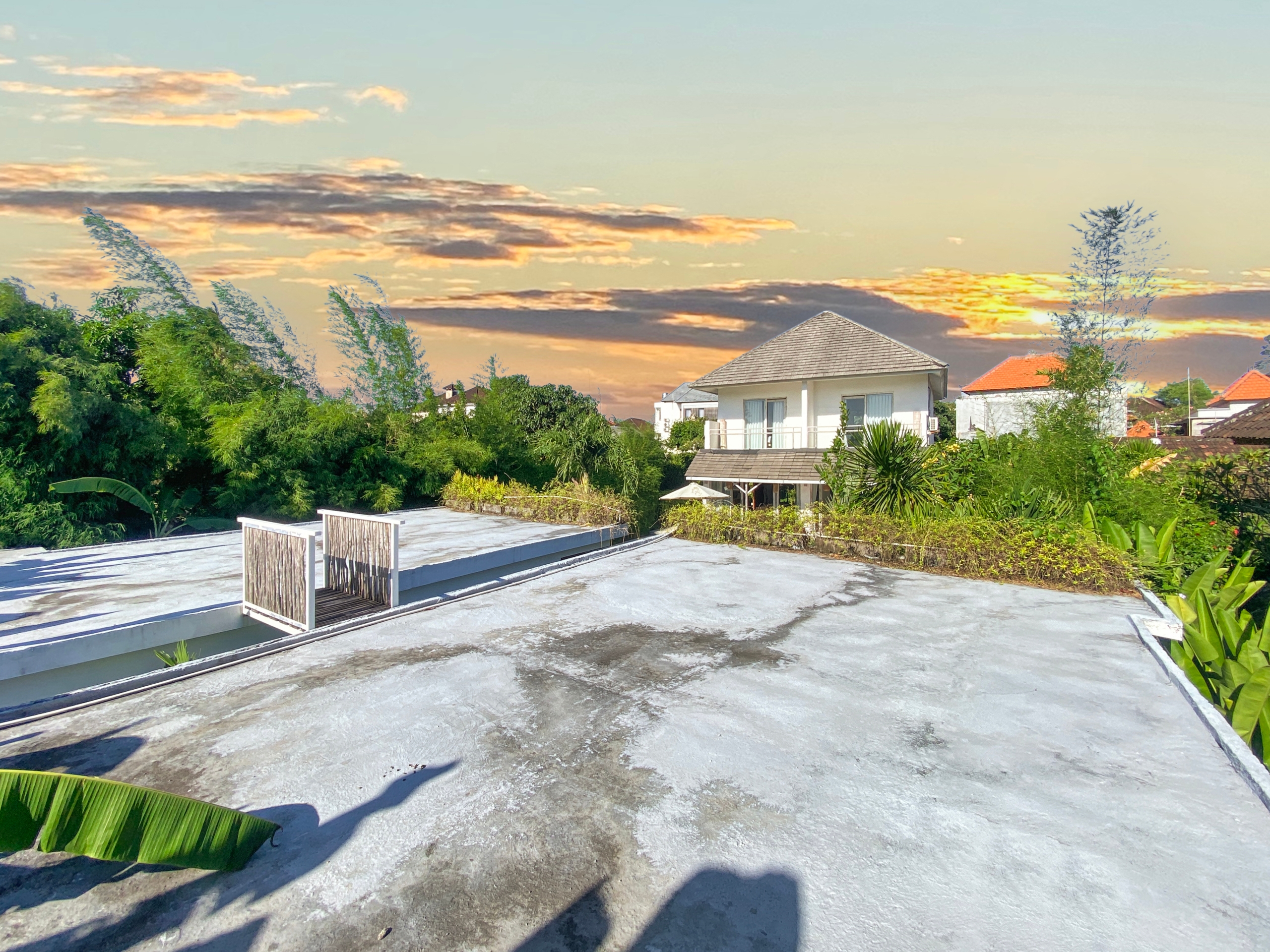 Rooftop terrace with white railings and lush greenery, overlooking suburban houses at sunset." (concise)