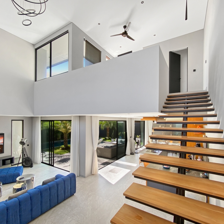 Bright open living room with floating wooden staircase, blue tufted sofa, and glass doors opening to a patio garden.