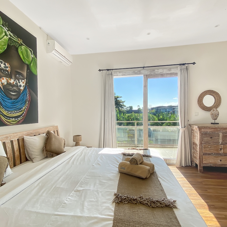 Bright bedroom with two beds, beige walls, and a large Maasai portrait above the bed.