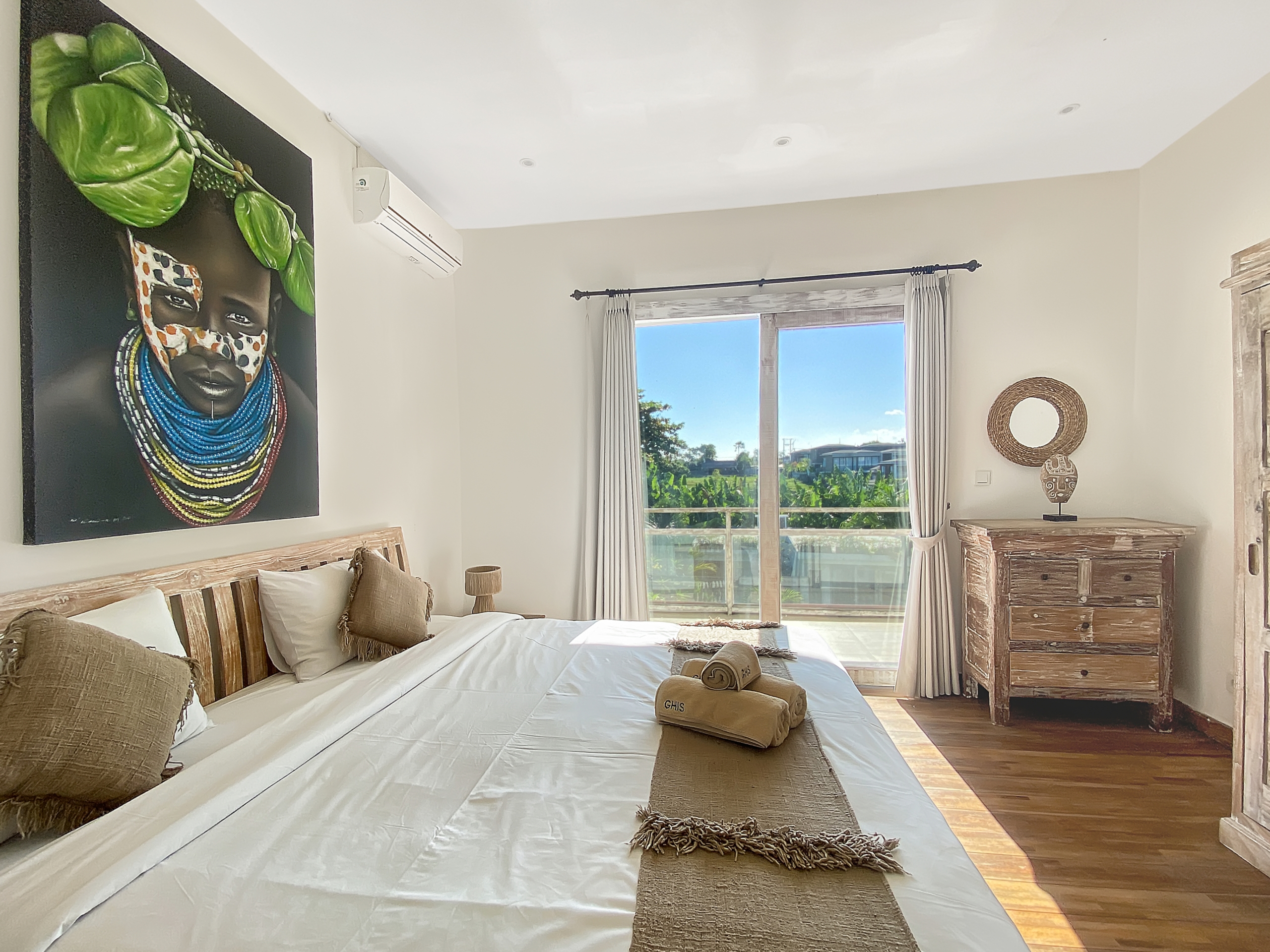 Bright bedroom with two beds, beige walls, and a large Maasai portrait above the bed.