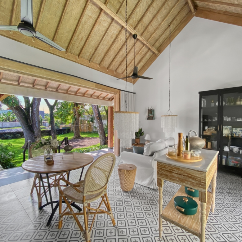Open living area with a thatched high ceiling, ceiling fans, and a view of a lush garden outside.