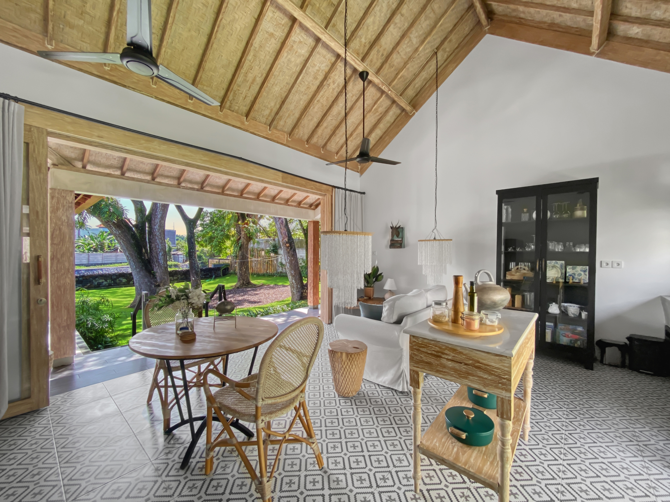 82a6a4514d947917b23200687b9c37ba129c099a Open living area with a thatched high ceiling, ceiling fans, and a view of a lush garden outside.