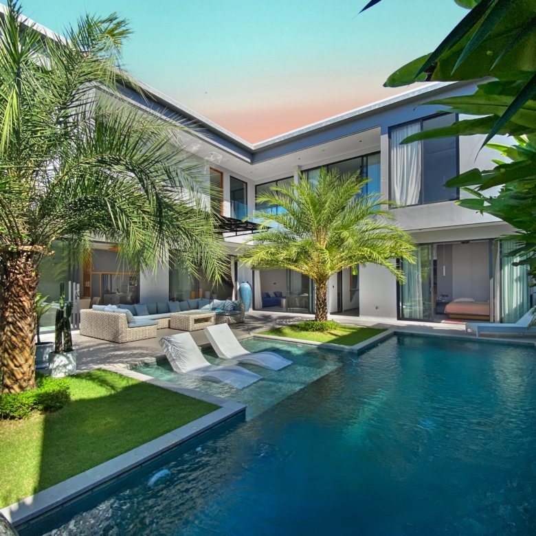 Contemporary house with glass walls, a rectangular pool, and palm trees in a sunny backyard.