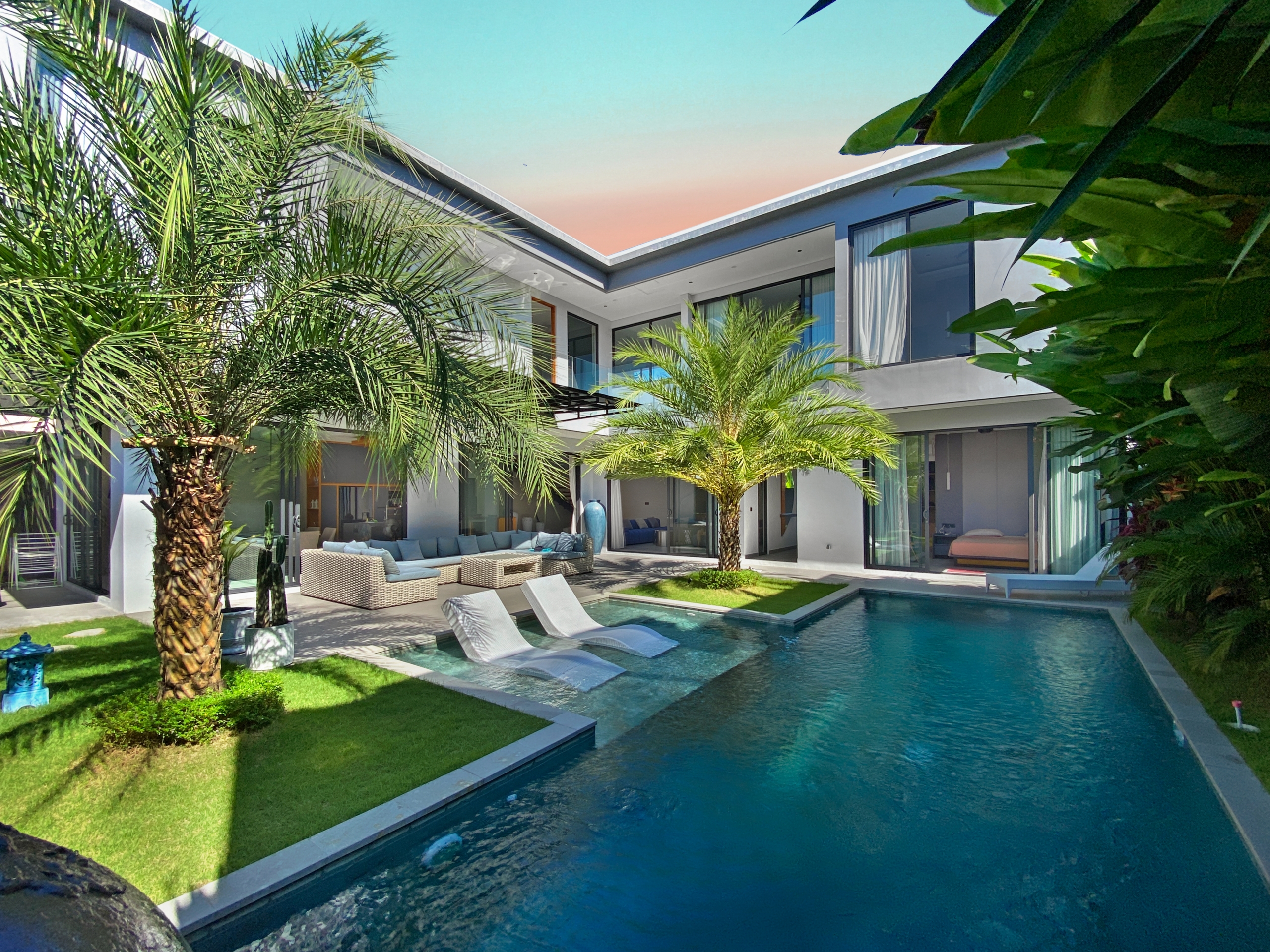 Contemporary house with glass walls, a rectangular pool, and palm trees in a sunny backyard.