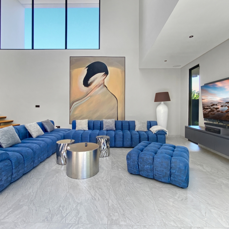 Modern living room with a bright blue modular sofa, abstract wall art, and a large flat-screen TV.