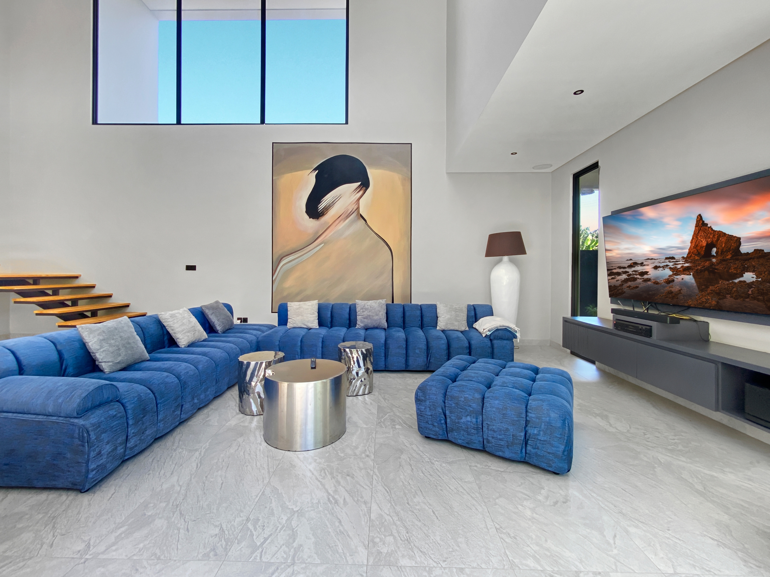 Modern living room with a bright blue modular sofa, abstract wall art, and a large flat-screen TV.