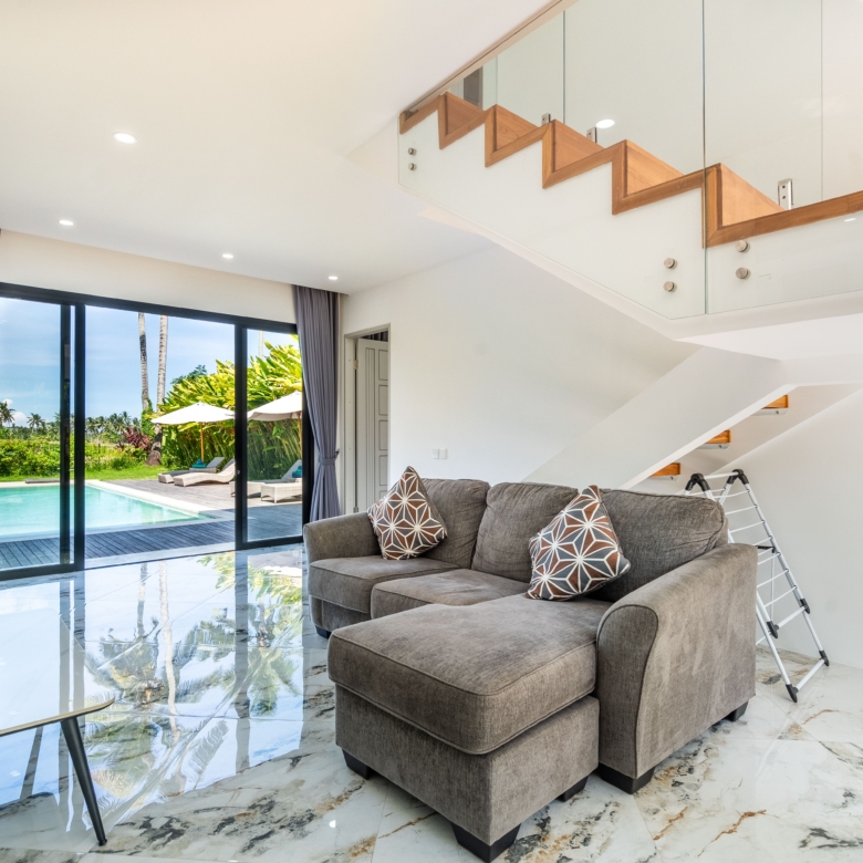 Modern living room with a gray sofa and patterned throw pillows, glass doors to a pool patio outside.