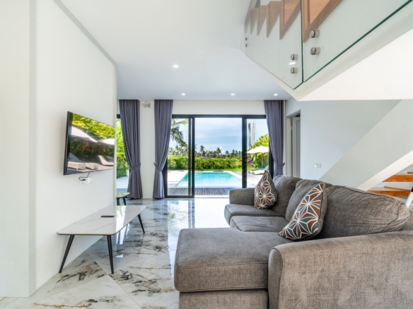 Modern living room with grey sectional, patterned throw pillows, and marble floor; large glass doors open to a sunny pool area outside.
