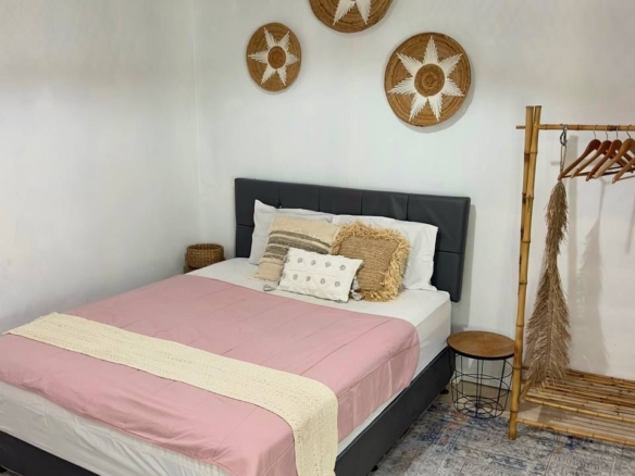 Cozy bedroom with a dark upholstered bed, pink bedspread, and cream knit throw; woven wall decor above.