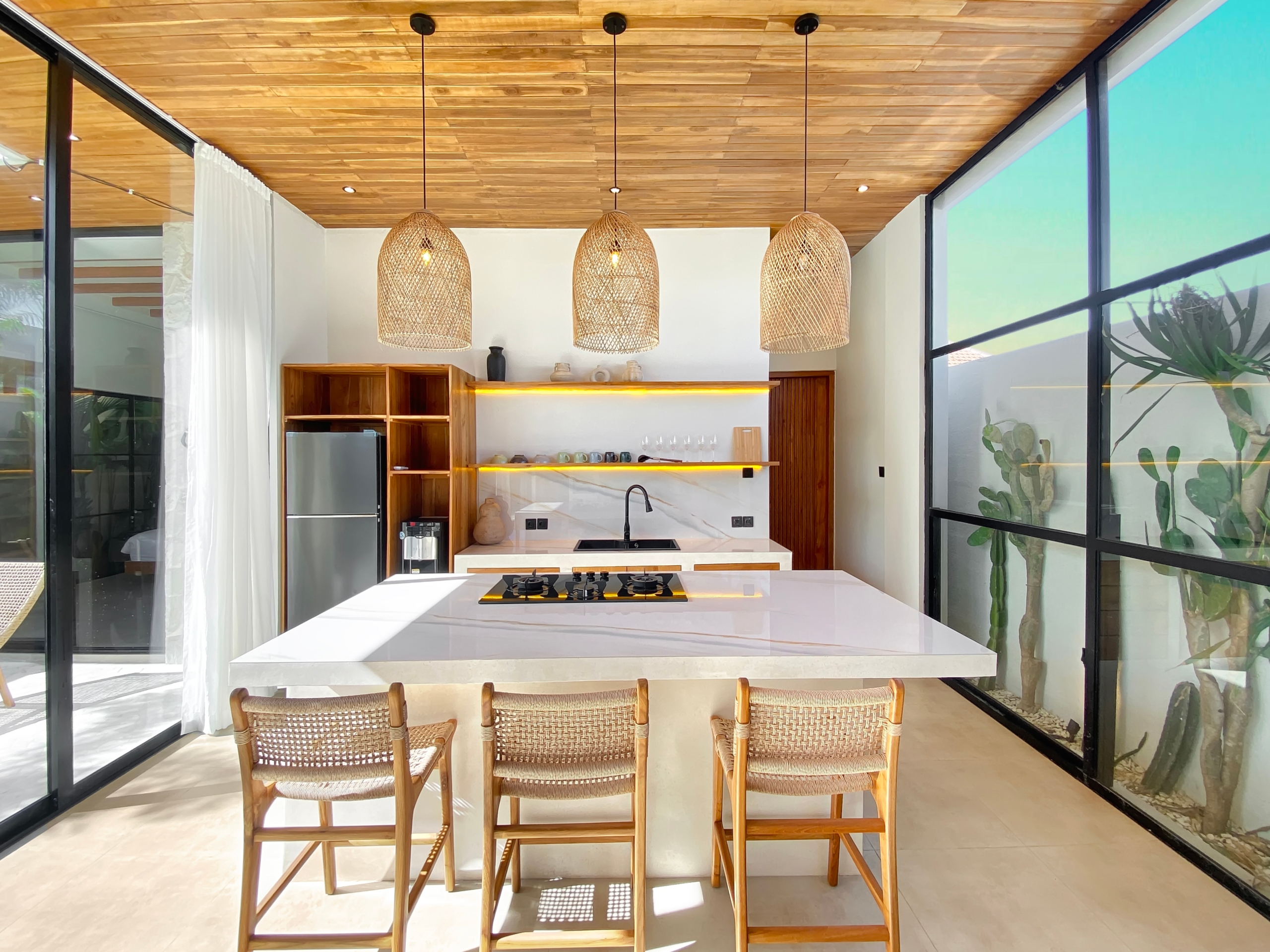 Open-plan kitchen with a white marble island, wooden cabinets, and three woven rattan pendant lights