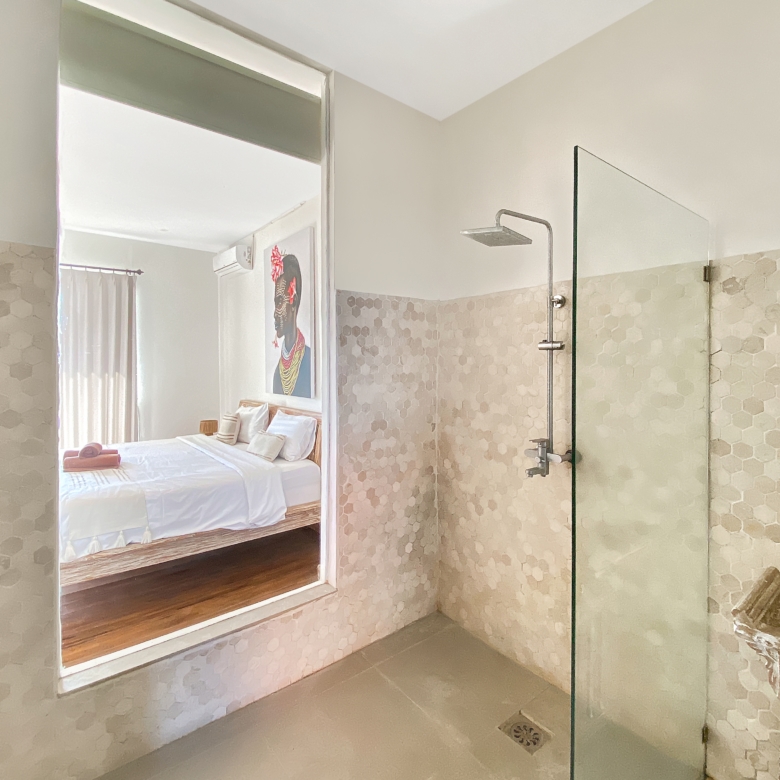 Bathroom with glass-enclosed shower and hexagonal tile walls leading to a bedroom through an open doorway. A rain shower head is visible on the right.