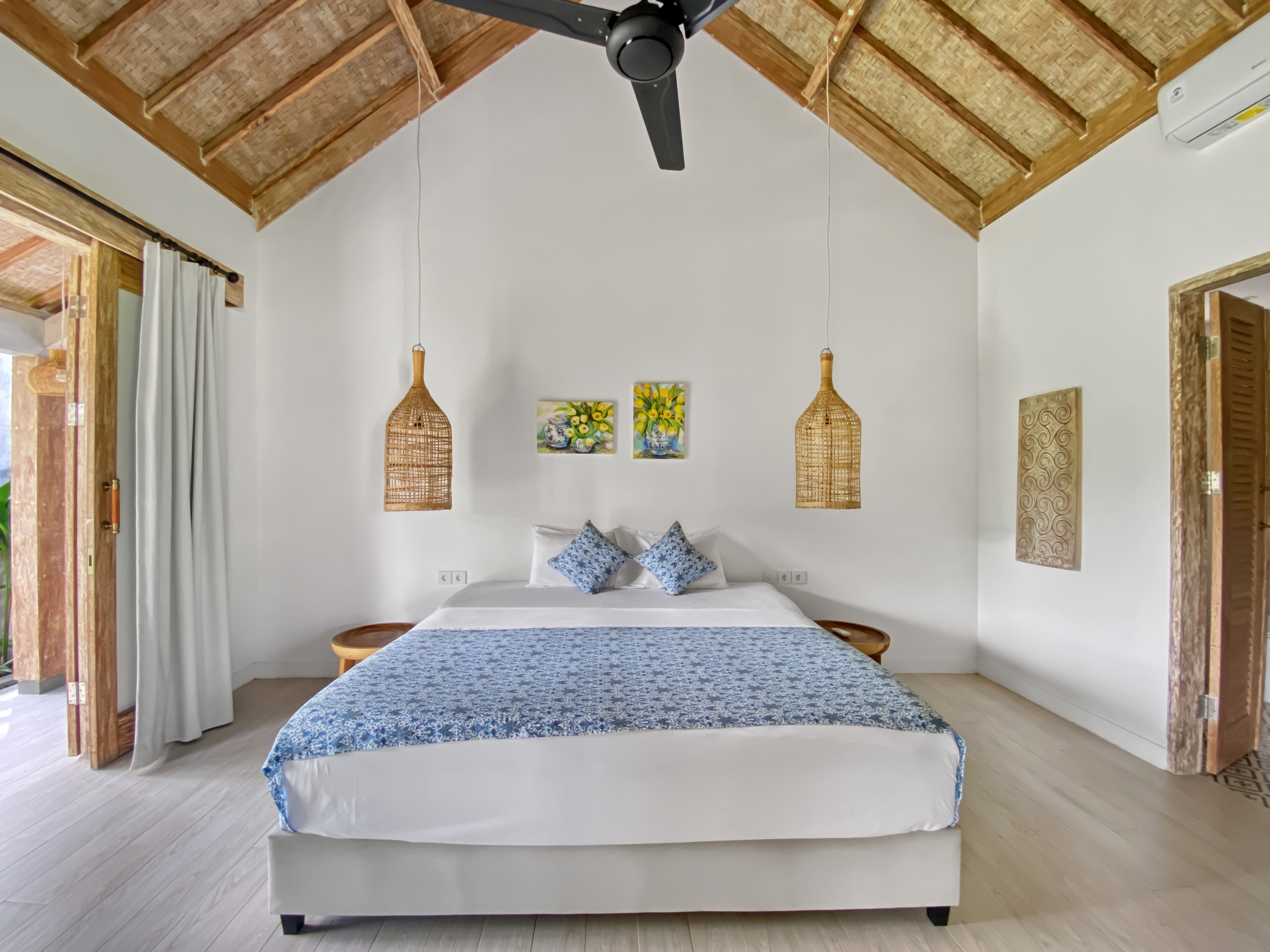 c818158e57a2d50cf9ea06131171475443c7efcd Bright bedroom with a large bed in white linens and a blue patterned throw, plus wicker pendant lamps and a thatched ceiling fan.