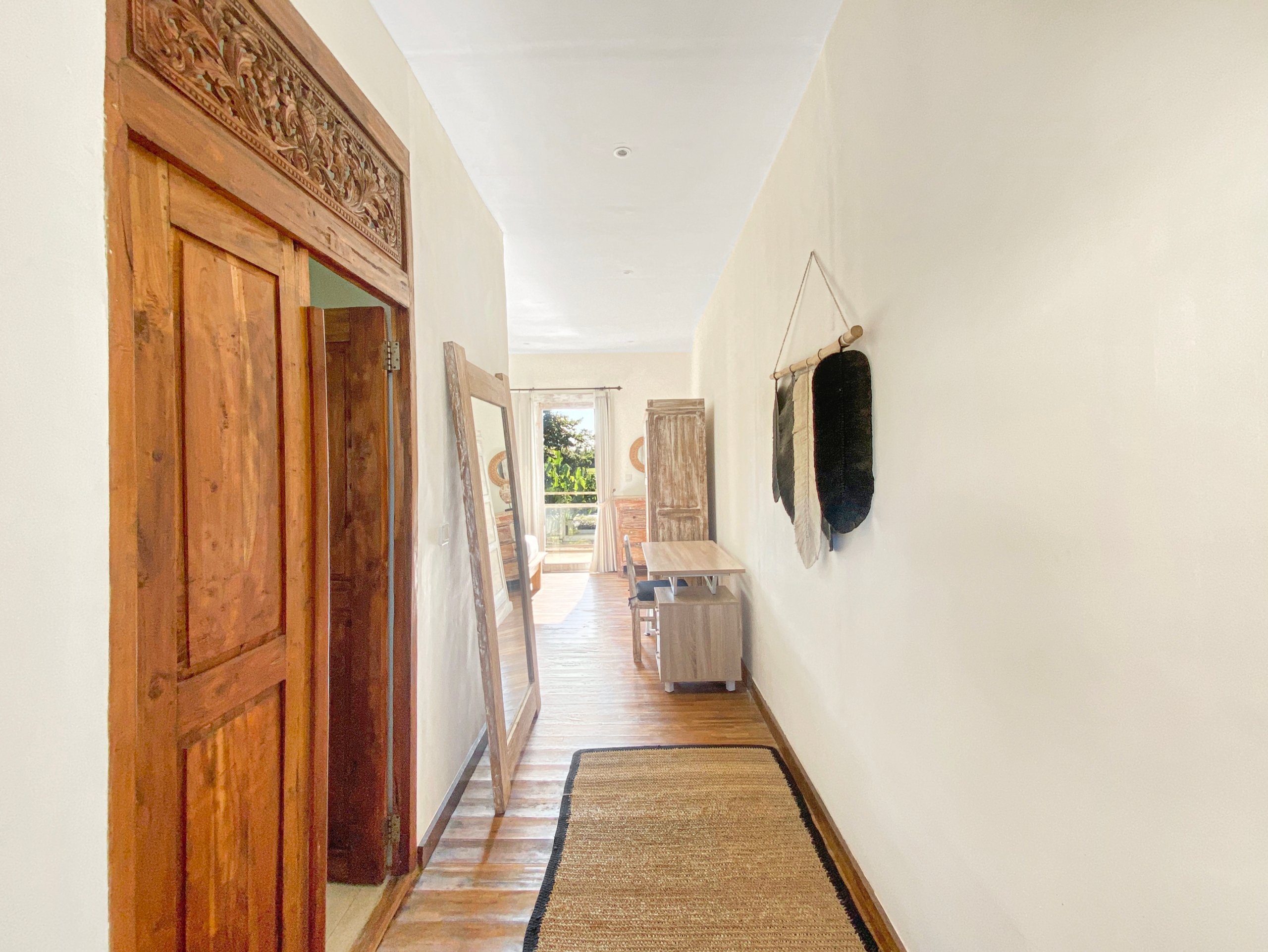 Long narrow hallway with a carved wooden door frame on the left and a sunlit view at the far end.