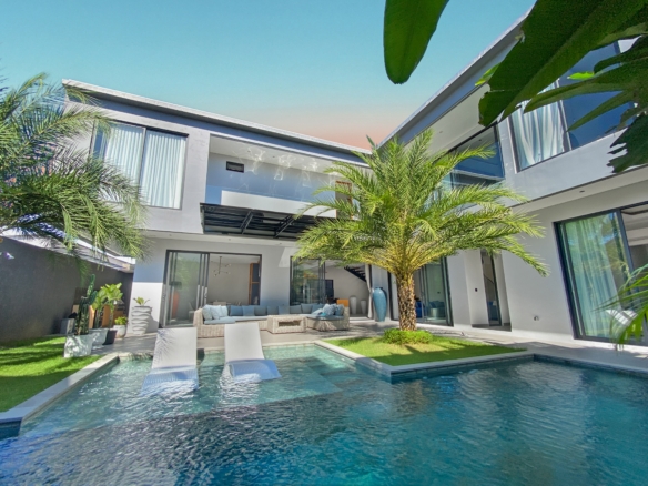 Modern two-story white house with glass doors, palm trees, and a rectangular pool with white loungers outside.