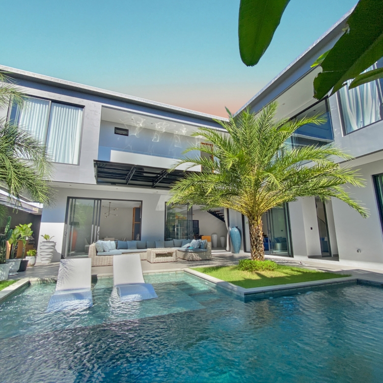 Modern two-story white house with glass doors, palm trees, and a rectangular pool with white loungers outside.