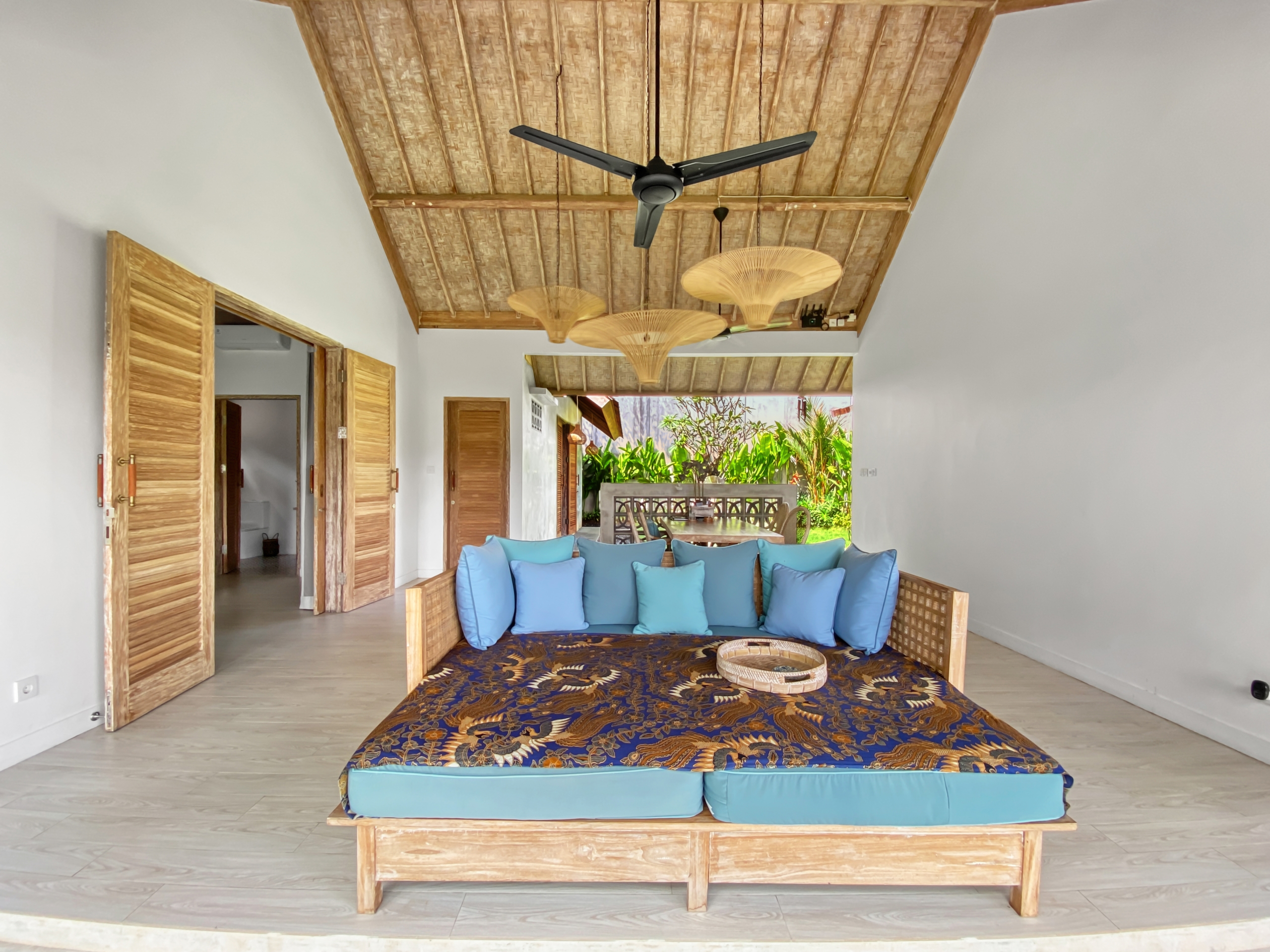 d55de0cd0315500045721a5eb3e13fee3caad65f Open-air living area with a blue-cushioned wicker sofa under a wooden thatched ceiling and ceiling fans.