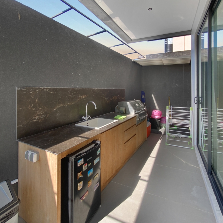 Outdoor balcony kitchen with dark stone backsplash, wooden cabinets, and a stainless steel grill next to a sink.