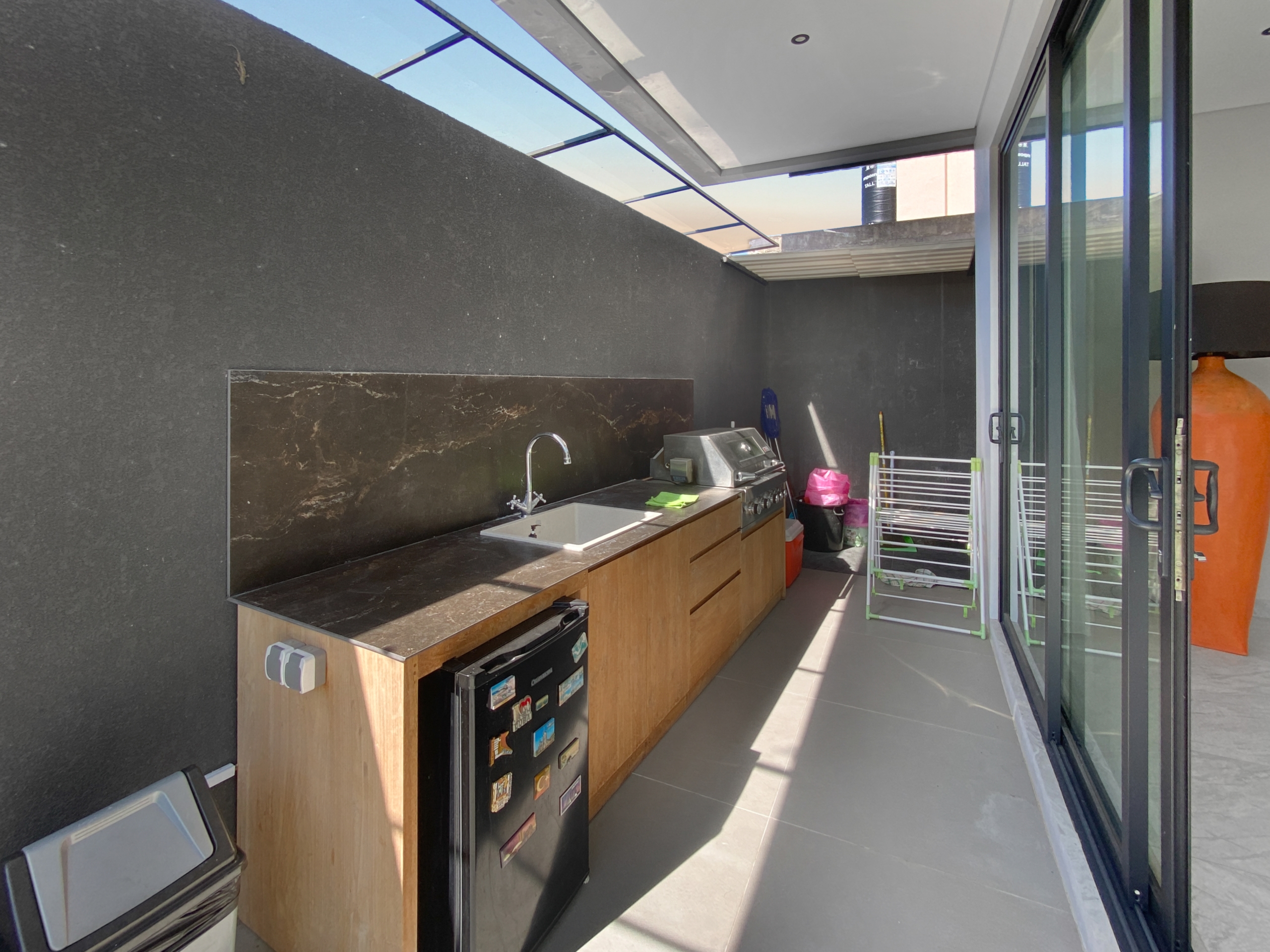 Outdoor balcony kitchen with dark stone backsplash, wooden cabinets, and a stainless steel grill next to a sink.