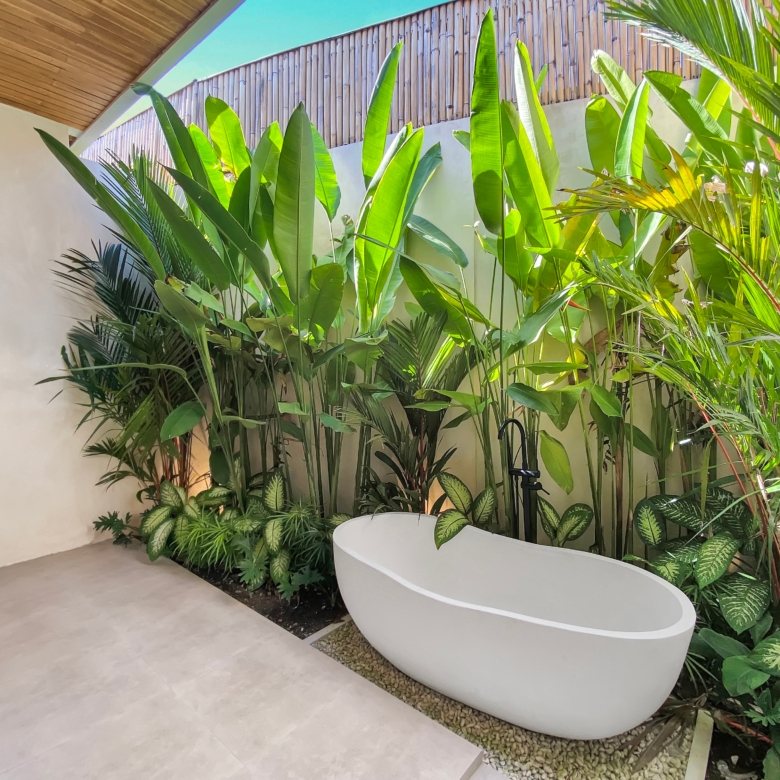 Indoor courtyard with a curved white planter filled with tall tropical plants along a beige wall and light tile floor, under a wooden ceiling.