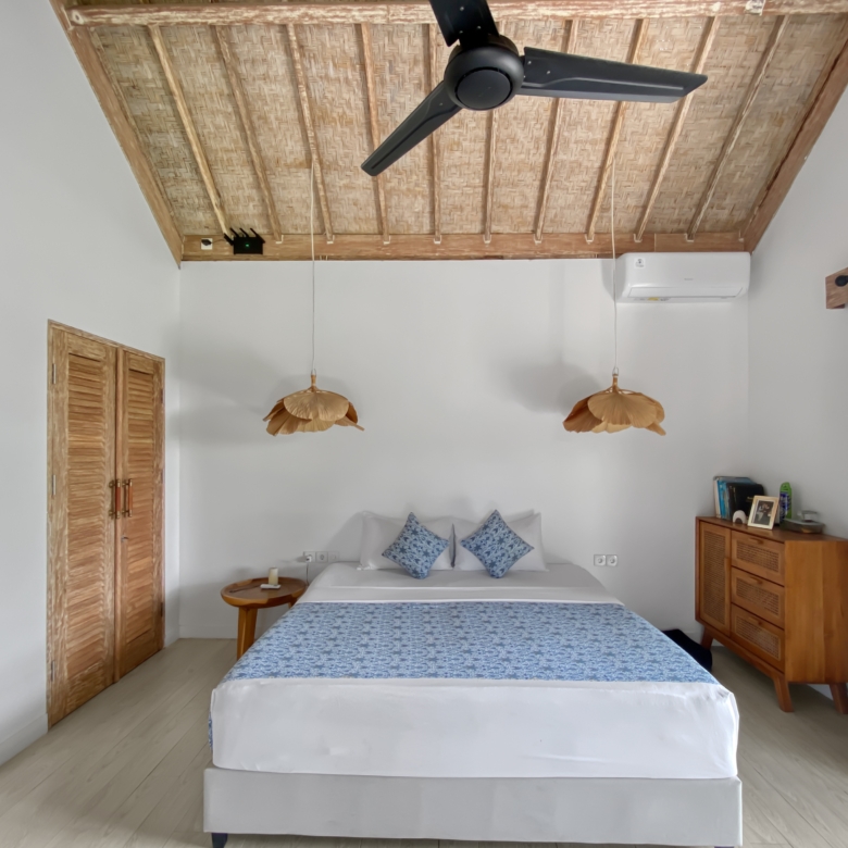 Bedroom with two twin beds pushed together, white bedding and blue patterned runners, and a wooden woven ceiling with a black ceiling fan.