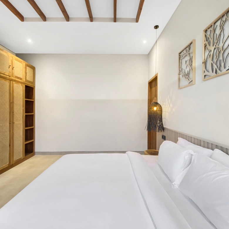 Hotel bedroom with white linens, a wooden headboard and wardrobe, and decorative wall art panels on the right.