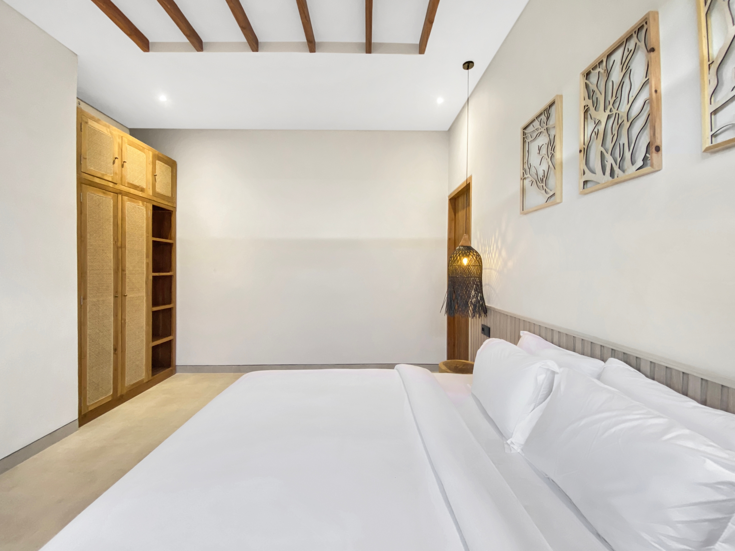 Hotel bedroom with white linens, a wooden headboard and wardrobe, and decorative wall art panels on the right.