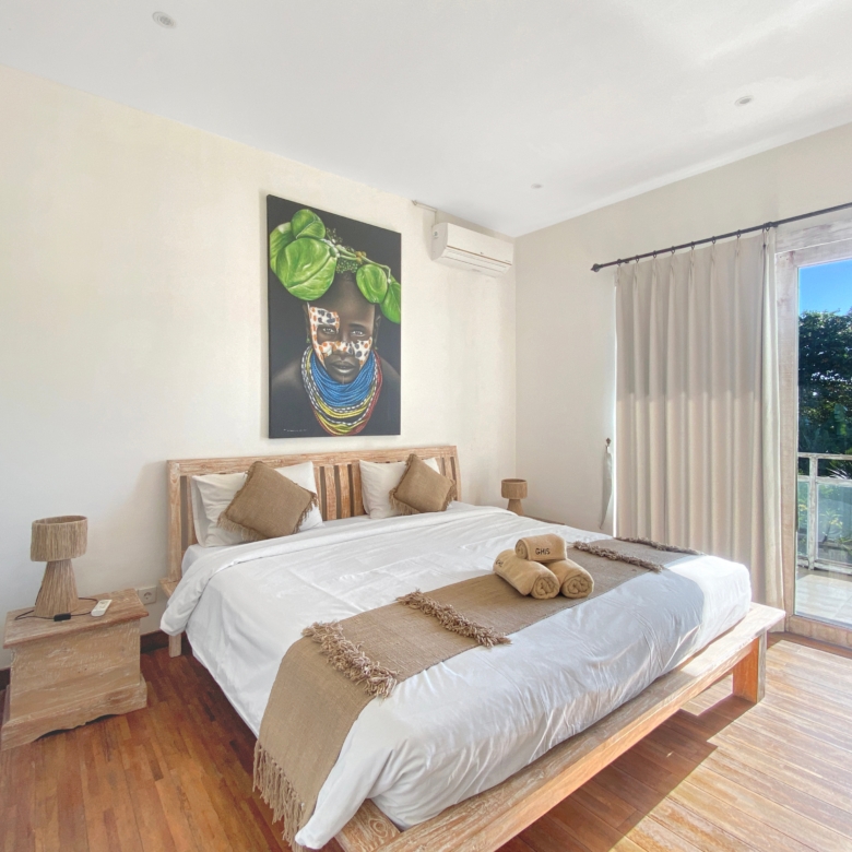 Bright bedroom with white bedding and a beige throw on a wooden bed, plus a bold wall art piece above the headboard.